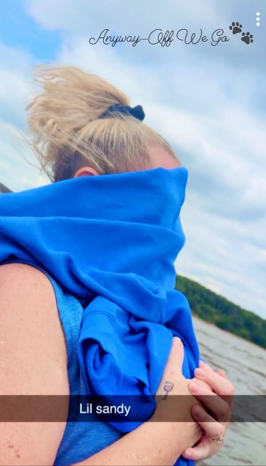 A person standing near water, partially covered with a blue fabric, with the caption 'Lil sandy' visible below.
