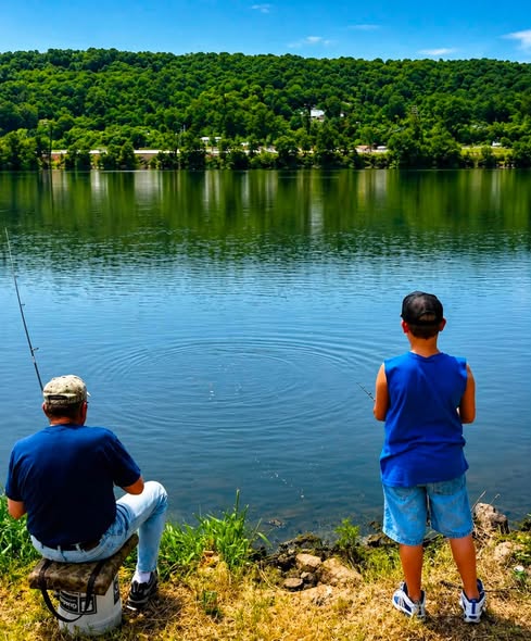 Two people fishing by a calm lake, with green hills in the background and water ripples visible.