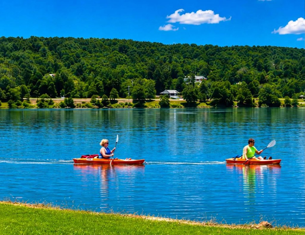 Two people kayaking on a calm lake surrounded by greenery under a clear blue sky.
